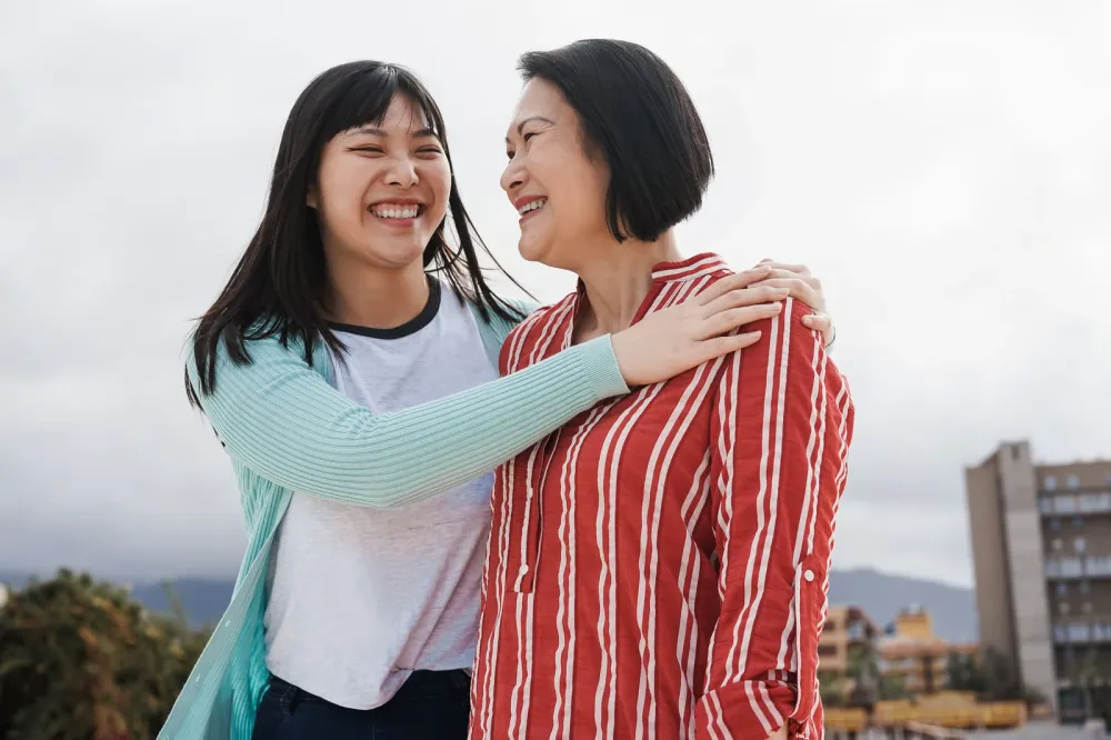 Two women laughing and hugging outdoors on a cloudy day
