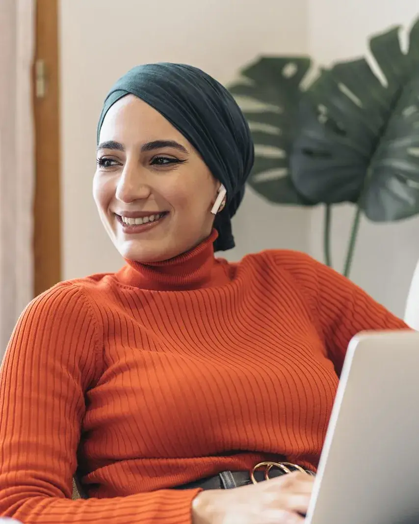 Woman in an orange jumper smiling on a sofa during a laptop video call