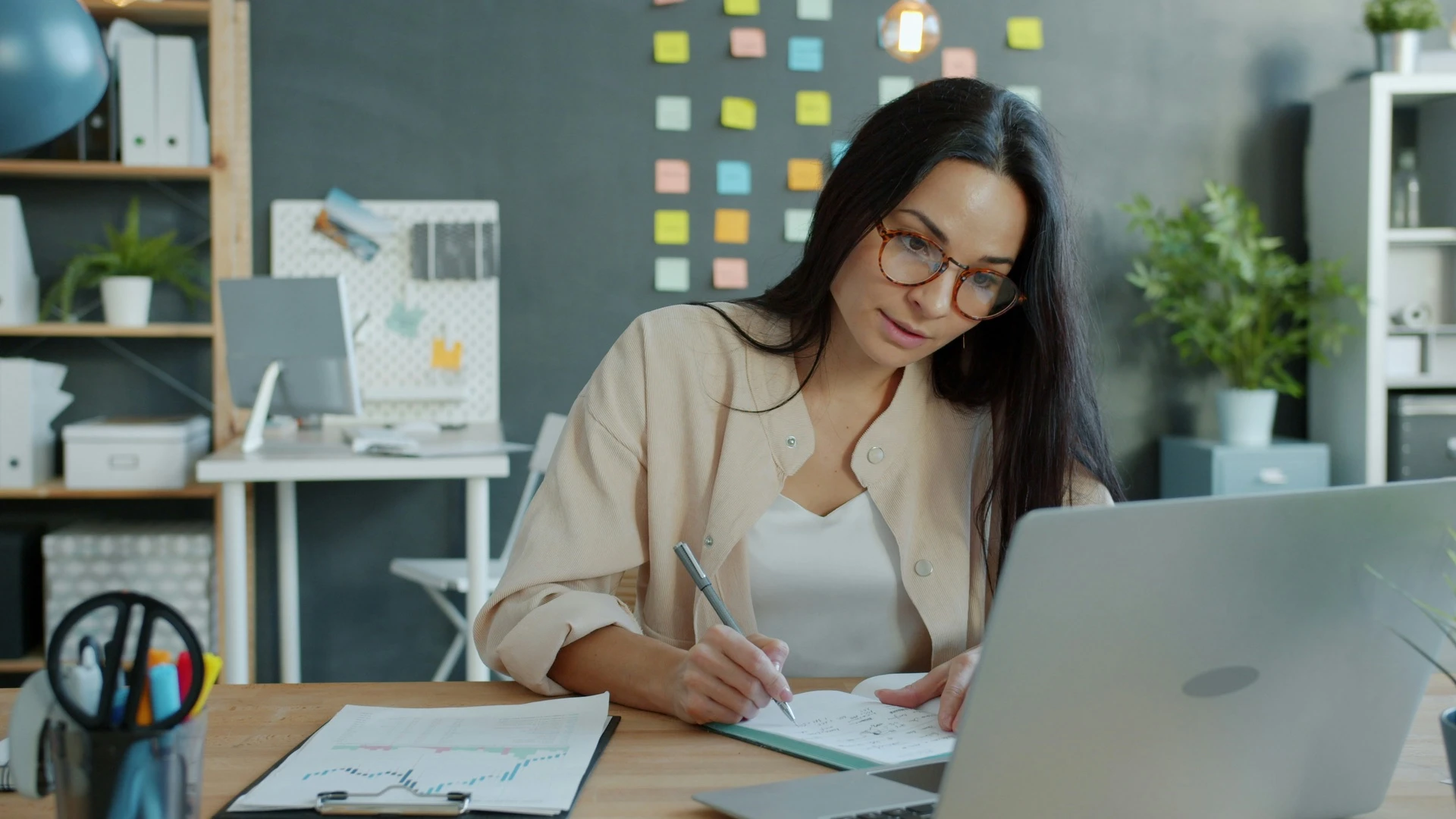 Woman writing notes in a notebook beside her laptop