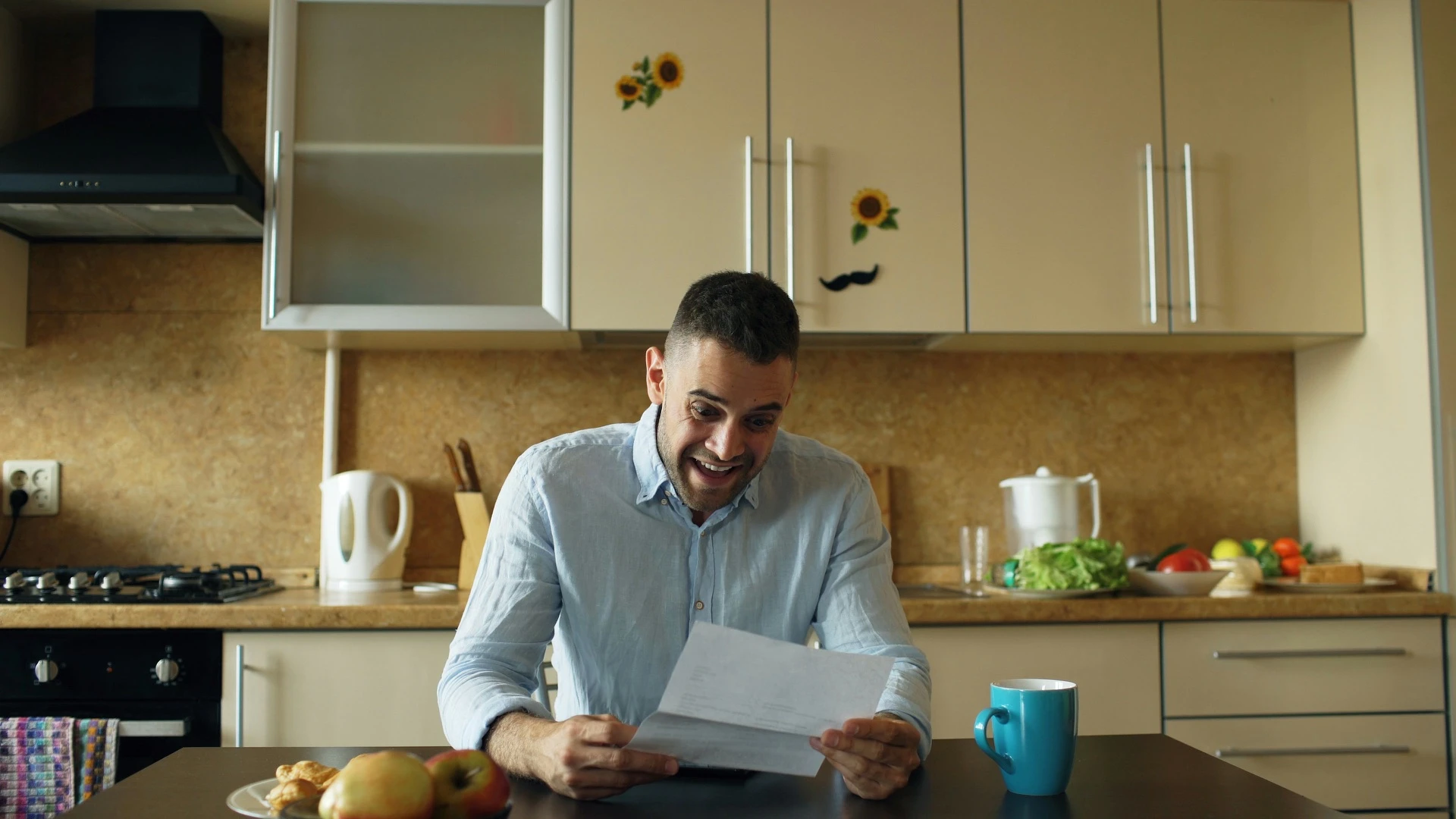 Man smiling as he reads a letter at his kitchen table