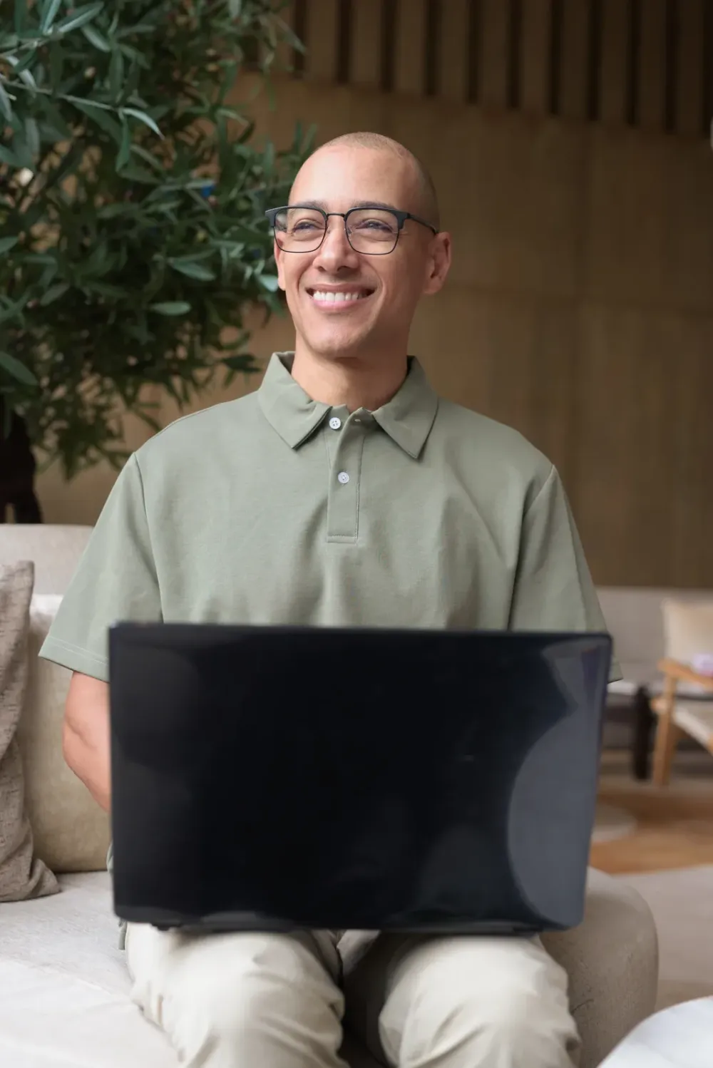 Smiling man sitting on a sofa with a laptop, joining a video session